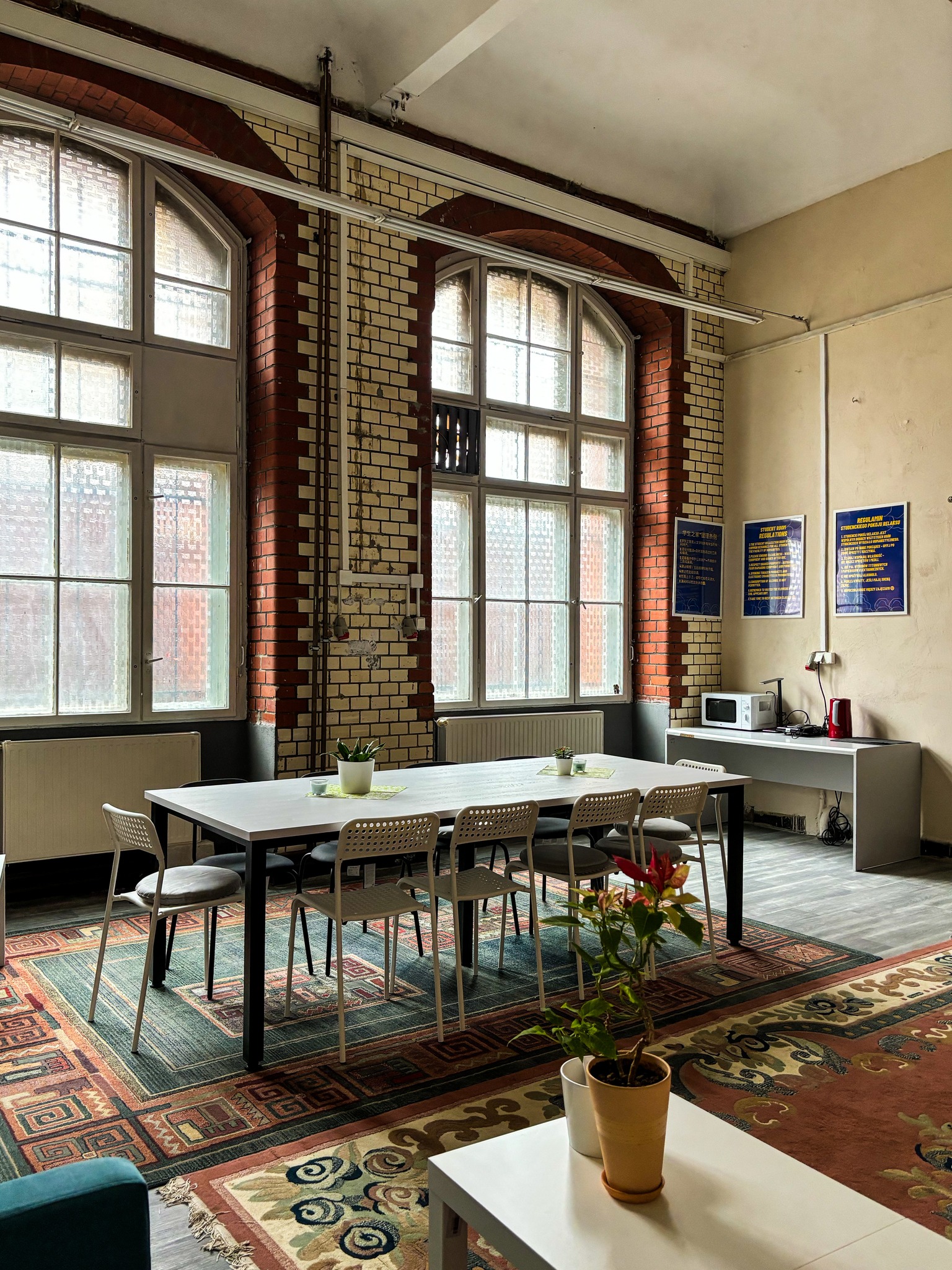 Strefa relaksu: duże okna, na środku duży st&oacute;ł z krzesłami i dywany na podłodze.